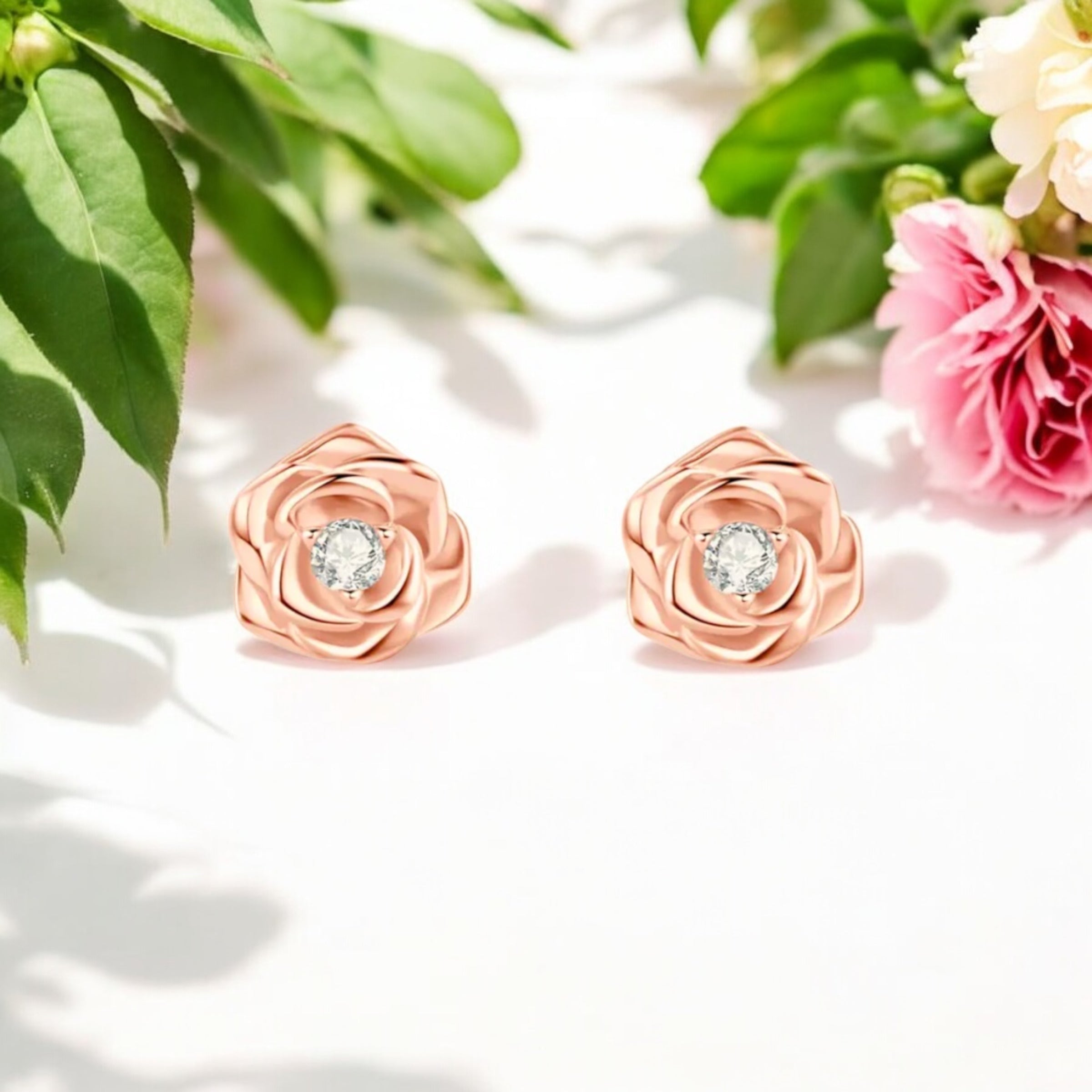 A pair of sculpted rose stud earrings in white gold or rose gold-plated sterling silver, each featuring a brilliant moissanite center stone.